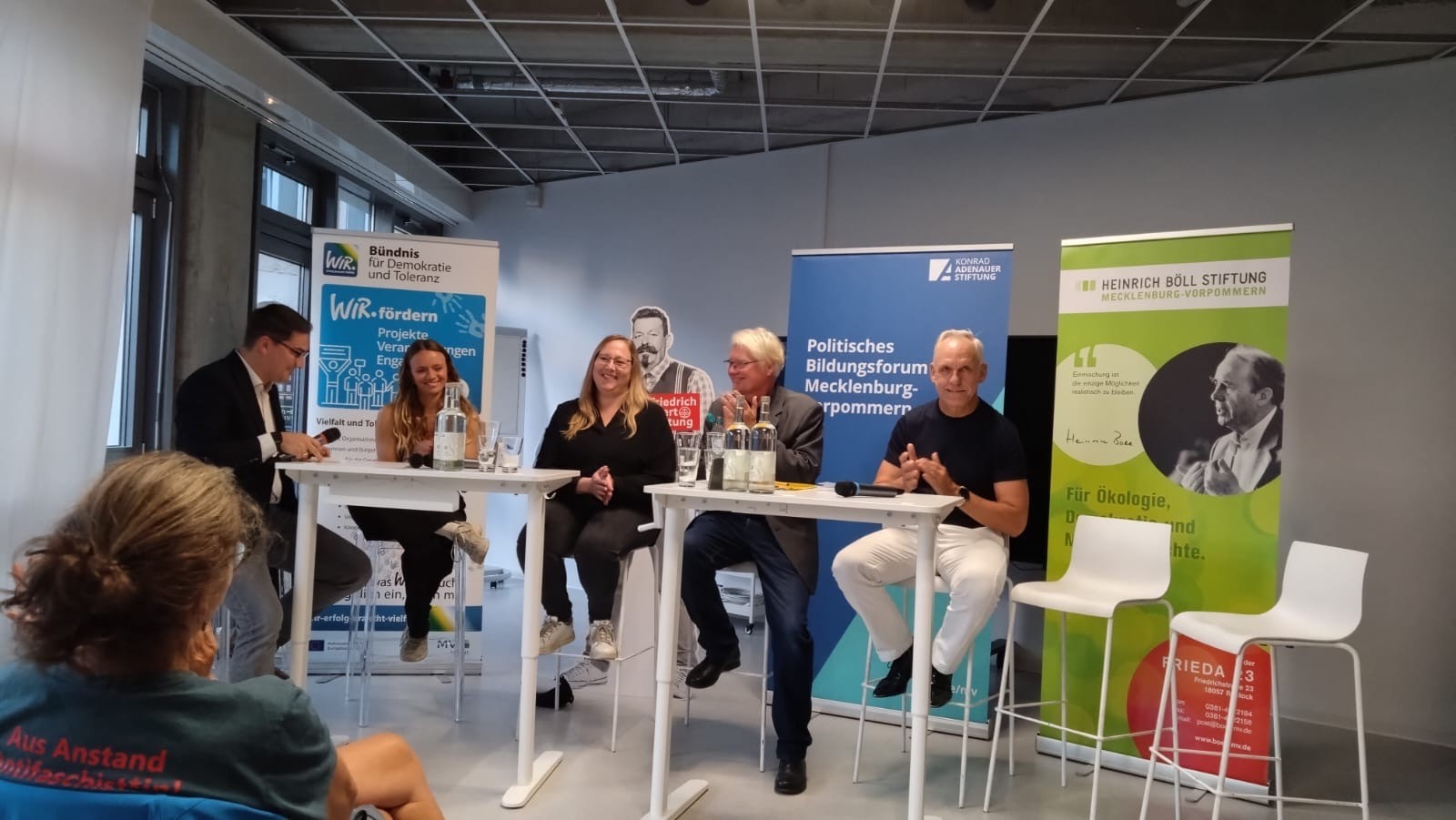 5 Personen sitzen an 2 Hochtischen vor Bannern der beteiligten Organisationen.