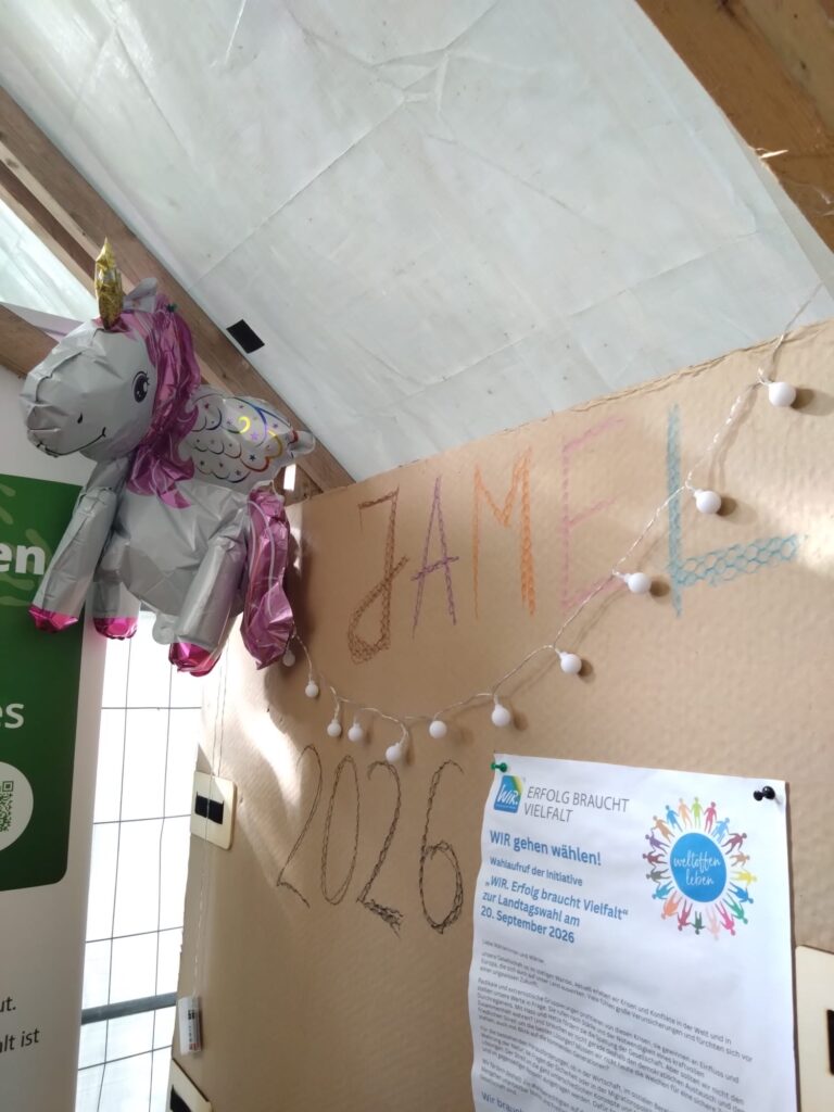 Stofftier und Lichterkette an einer Holzwand mit beschrifteter Pappe und einem Infoblatt.