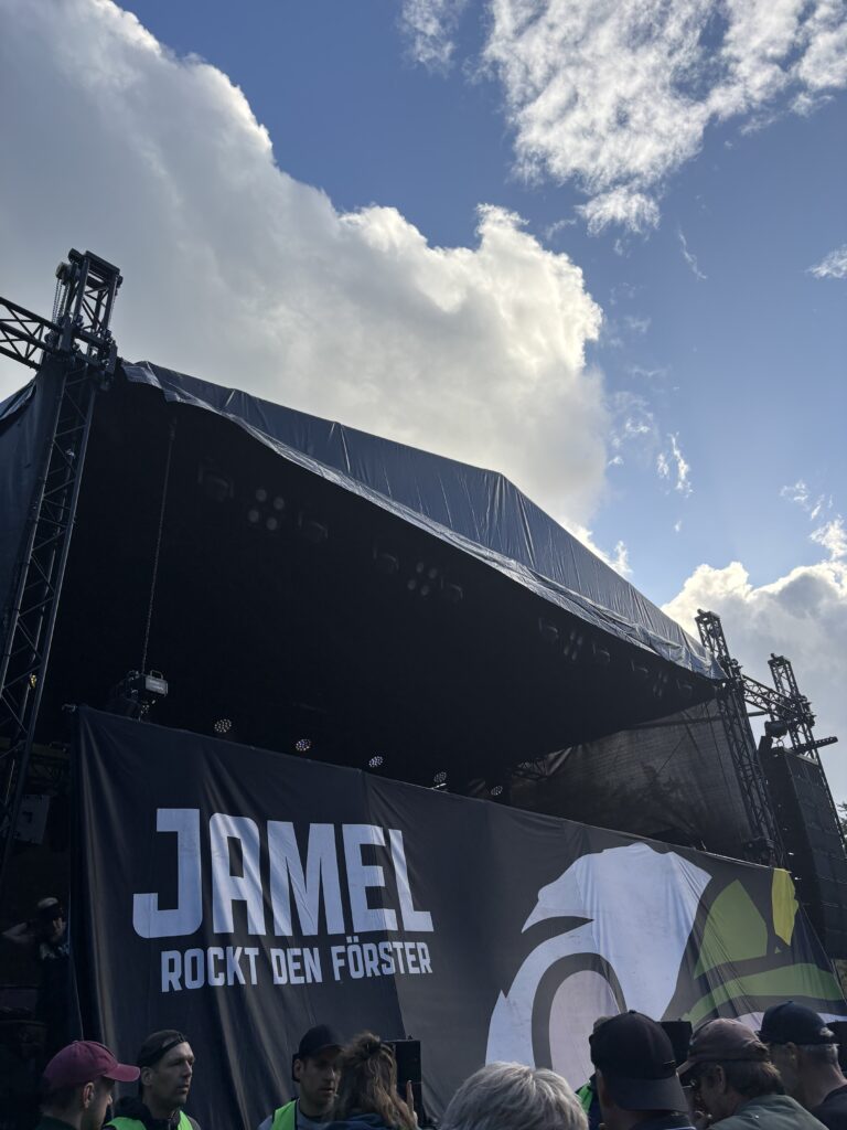Festivalbühne mit Jamel Banner unter blauem Himmel und großen Wolken.