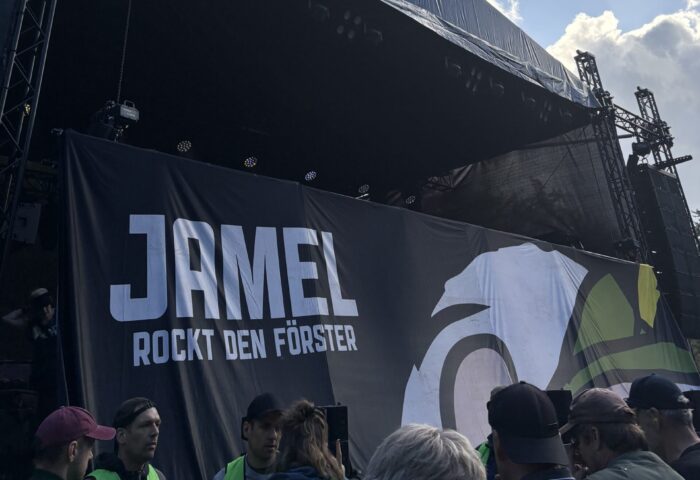 Festivalbühne mit Jamel Banner unter blauem Himmel und großen Wolken.